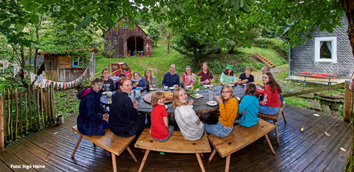 Eine Gruppe Menschen sitzt unter einem Baum im Kreis am Tisch